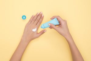 Close up of female hands on yellow background using hand moisturiser in blue tube