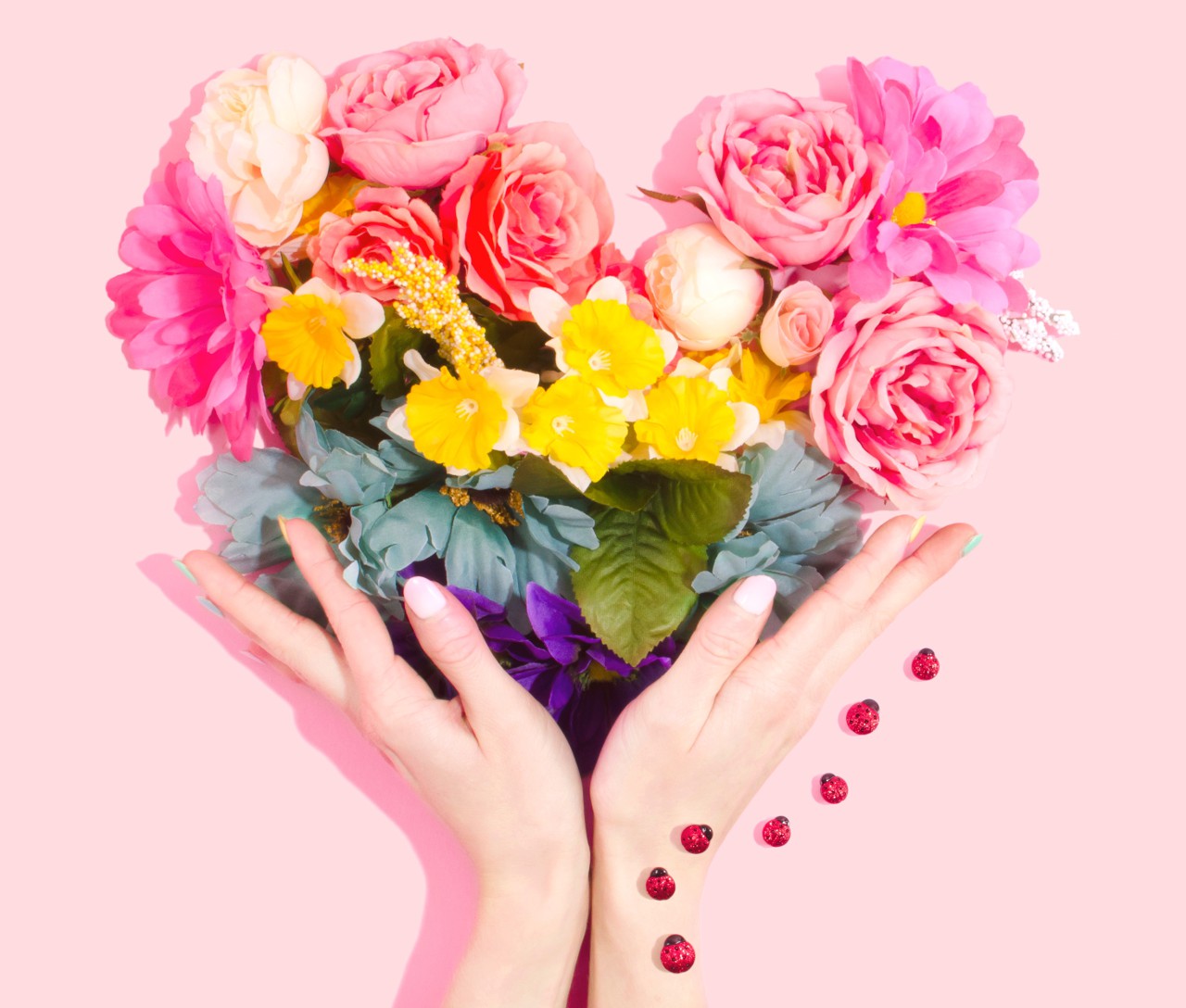 Open female hands holding bouquet of flowers in heart shape, with lady birds