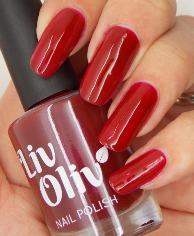 Close up female hand holding LivOliv scarlett red nail polish