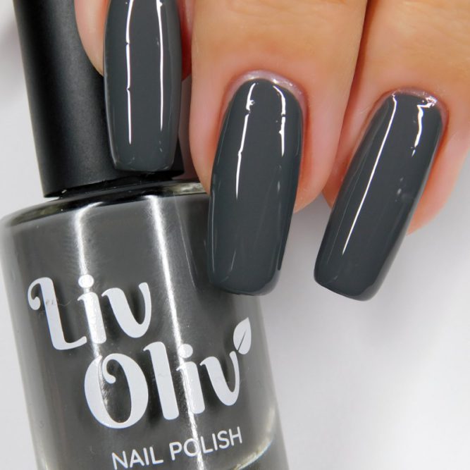 Close up of nails painted charcoal grey holding LivOliv 'Charlotte' nail polish bottle